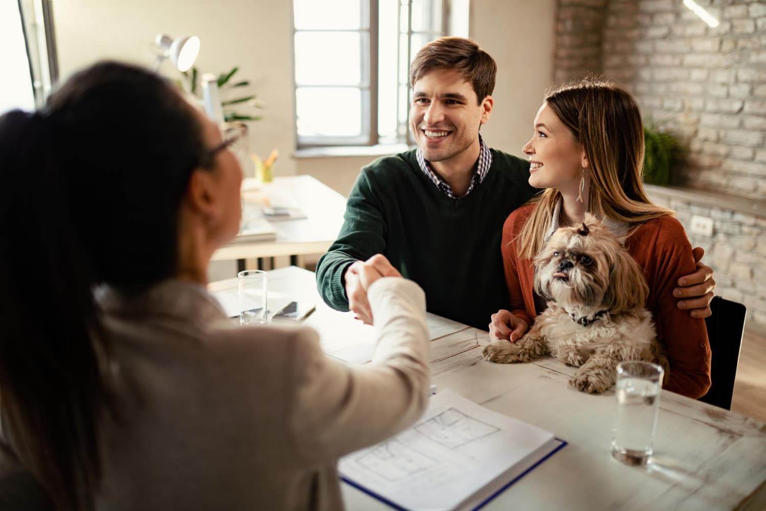 couple with dog shaking hands with real estate agent office